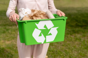 Woman holding a green recycling bin with a recycle symbol.