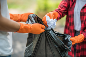 Two individuals, one in orange gloves, exchanging a filled black garbage bag