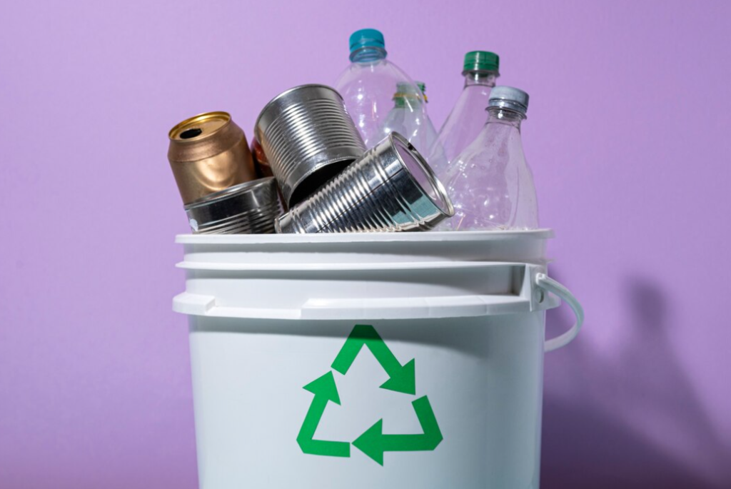 cans and plastic bottles in white bin adorned with a green recycling logo